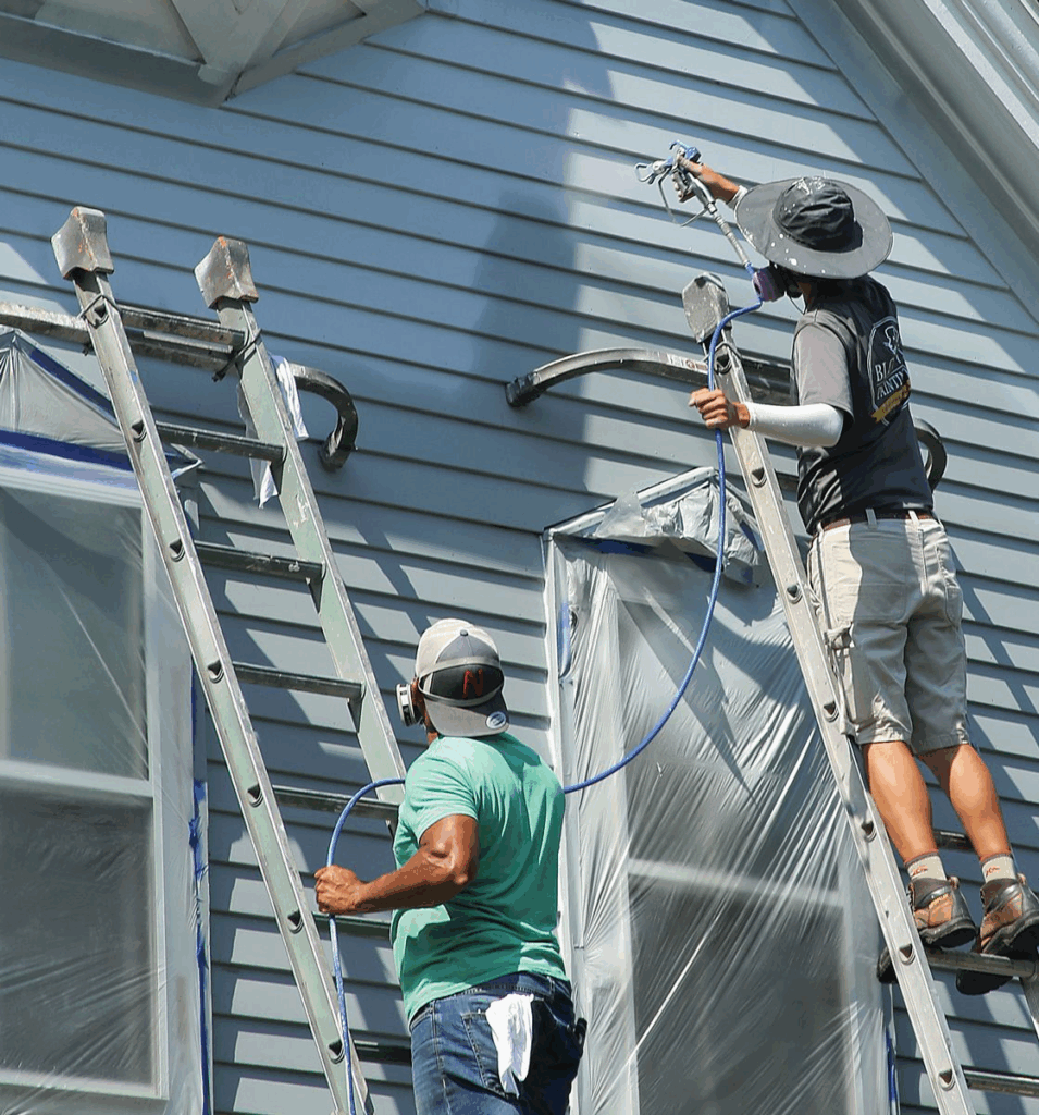 Workers painting blue house siding with professional spray equipment